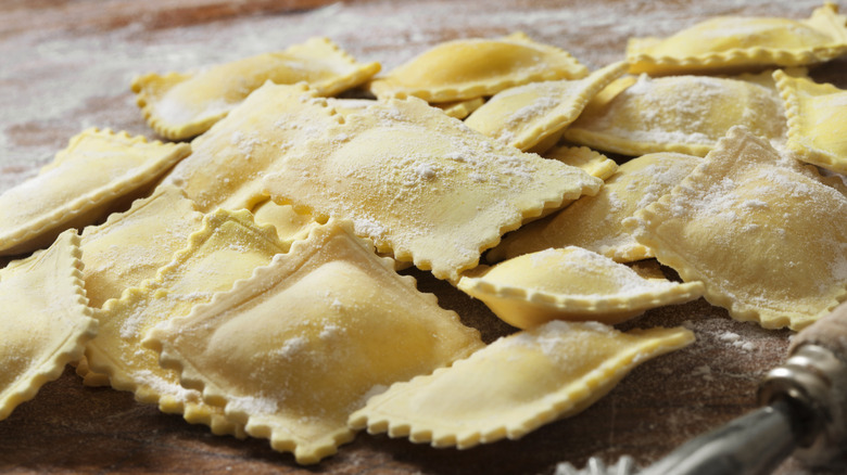 Square ravioli on a wooden surface dusted with flour.