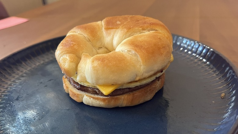 Close up of a Jimmy Dean Croissant Sandwich with Sausage, Egg & Cheese on a blue plate sitting on a wooden table