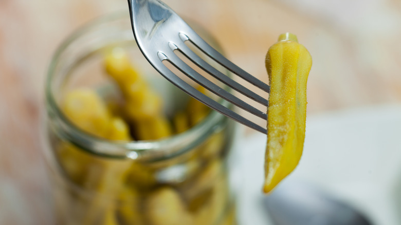 Pickled okra on the end of a fork, jar in background