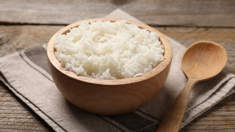 Cooked white rice in wooden bowl next to a wooden spoon