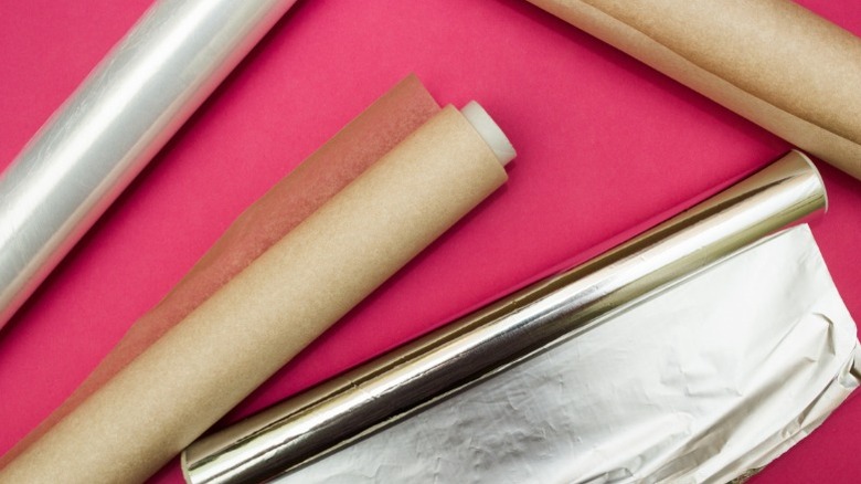 Rolls of parchment paper, aluminum foil, and plastic wrap on pink background