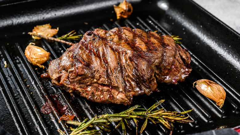 Flat iron steak on grill pan with garlic cloves and rosemary