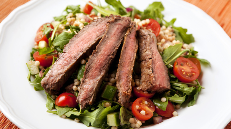 Sliced steak on salad in white bowl