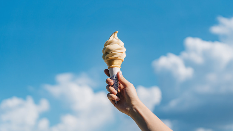 holding soft serve ice cream over blue sky