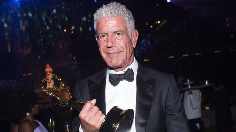 Anthony Bourdain smirking while holding an Emmy Award in a tuxedo