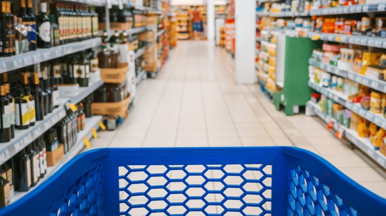 End of a blue grocery cart heading down a grocery aisle