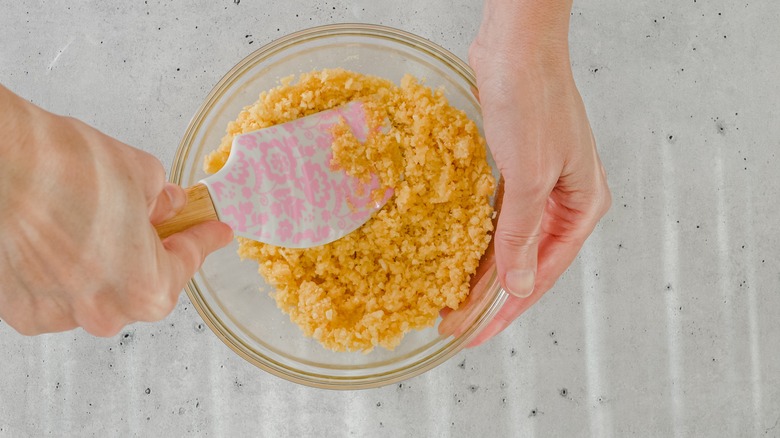 Hand holding spatula mixing butter into crushed graham crackers