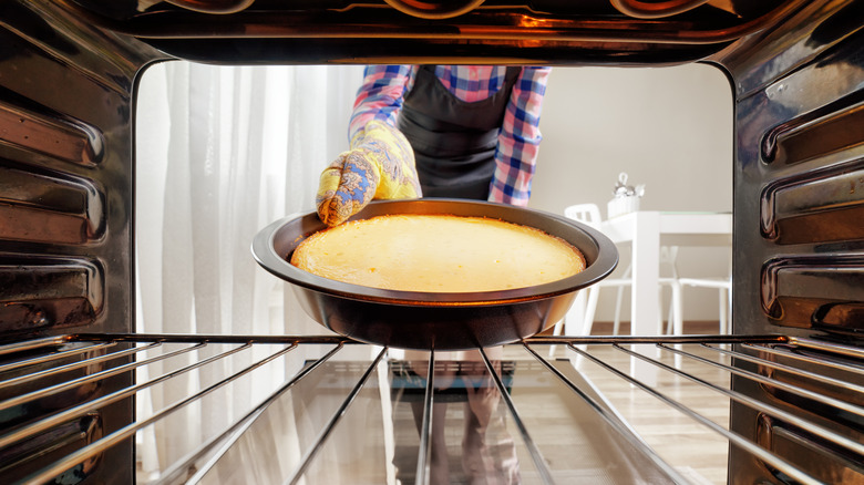 Hand in oven glove taking cheesecake out of oven