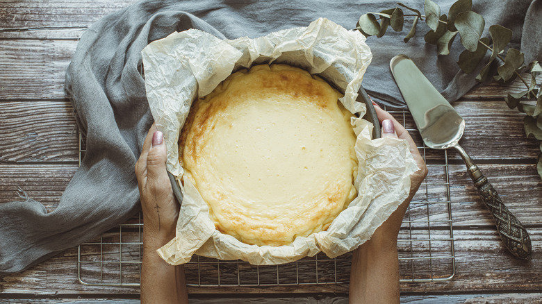 Hands holding a freshly-baked cheesecake in a tin