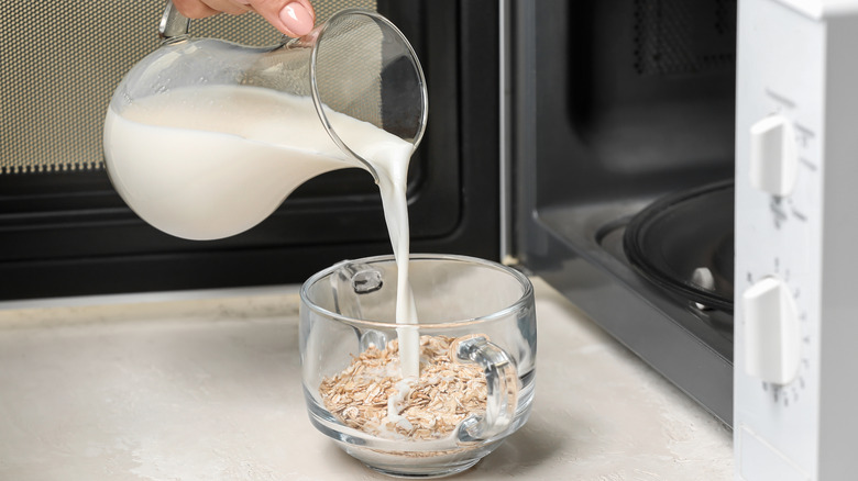 Person pouring milk into oatmeal from glass pitcher