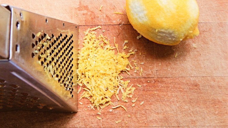 Lemon zest on wooden board next to grater