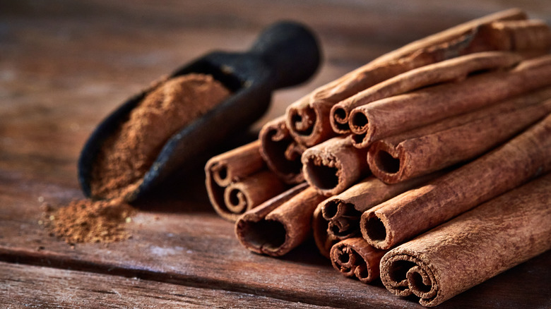 Ground cinnamon alongside cinnamon sticks on wooden table