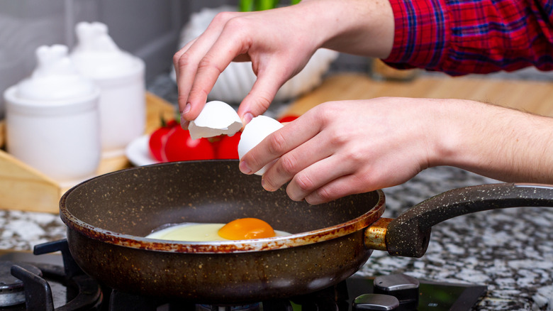 Hands cracking egg directly over frying pan