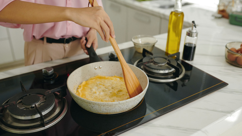 Person making omelet in a ceramic frying pan on a stove