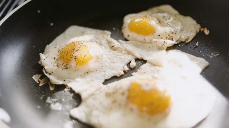 Three fried eggs cooking in a skillet