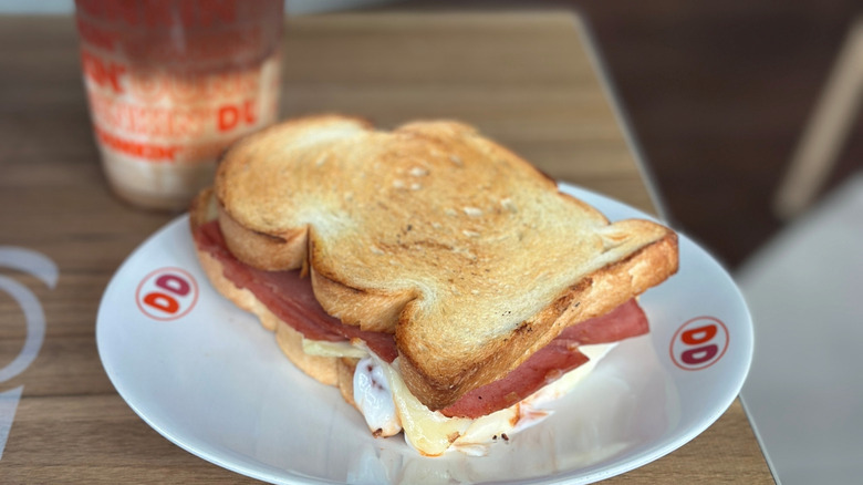 Stock photo of a Dunkin' toasted ham and cheese sandwich next to a cup of coffee.