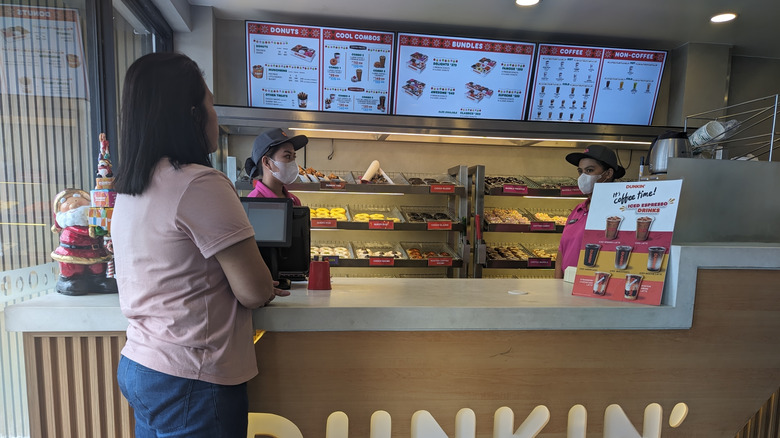 A stock photo of a customer talking to two employees at a Dunkin' coffee shop.