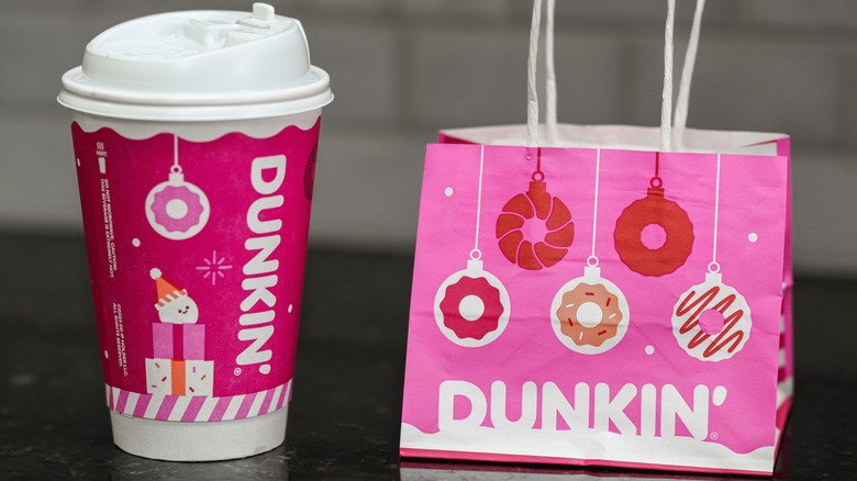 A stock photo of a seasonal Dunkin' coffee, next to a Dunkin' gift bag.