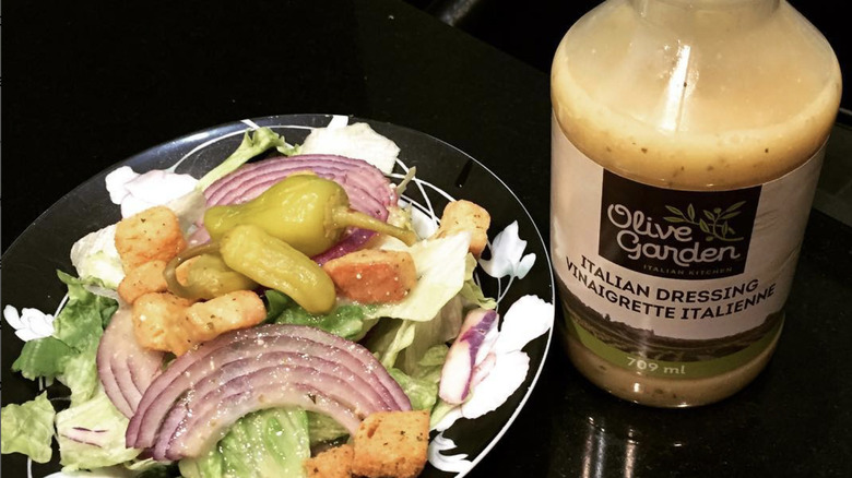 Olive Garden dressing bottle with salad on black plate