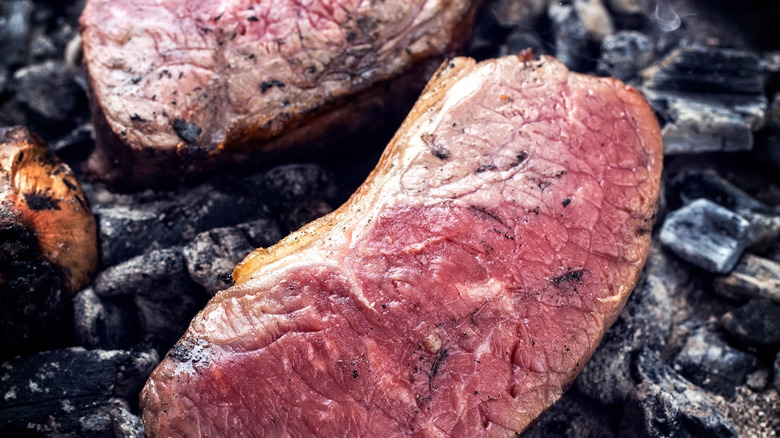 Steaks being cooked directly on charcoal.