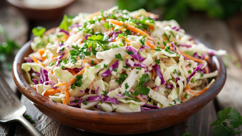 A wooden bowl of coleslaw with a fork next to it.