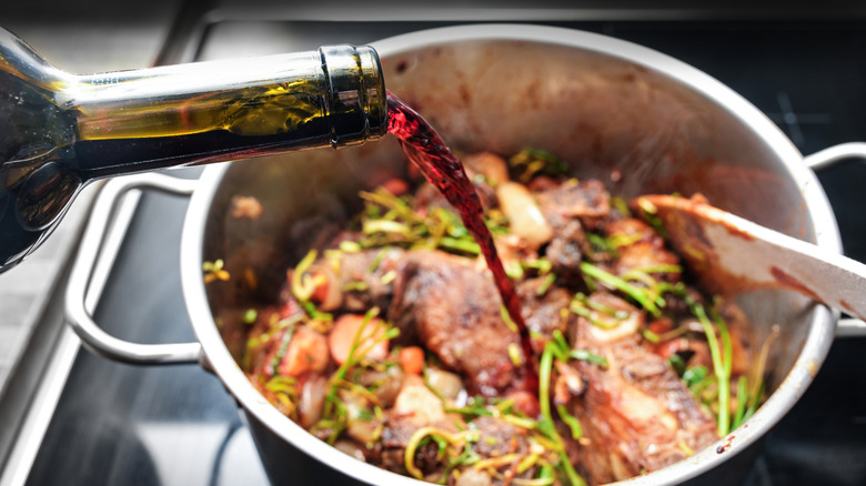 A cook pouring red wine into a pot with meat and vegetables