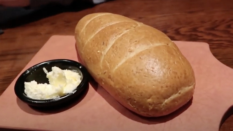 Loaf of Longhorn Steakhouse bread with whipped butter on the side, served on a wooden cutting board