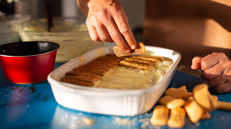 A baking dish with hands making tiramisu