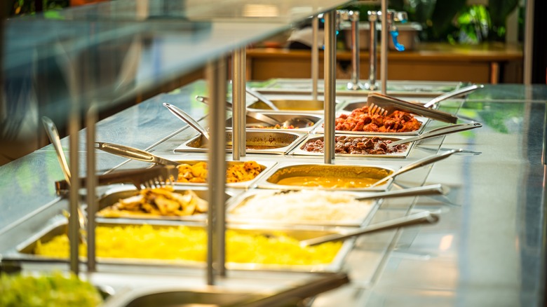 Buffet kiosk of Chinese food with tongs and spoons in the food dishes