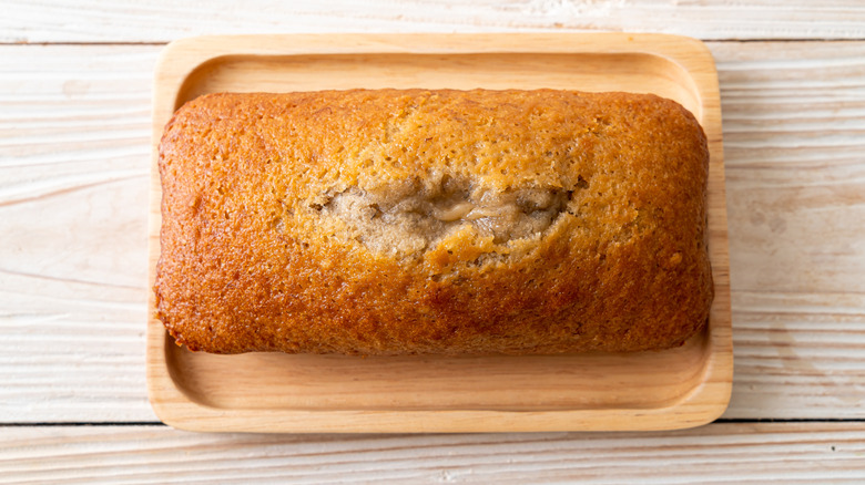 A loaf of banana bread with a center split on a wooden tray