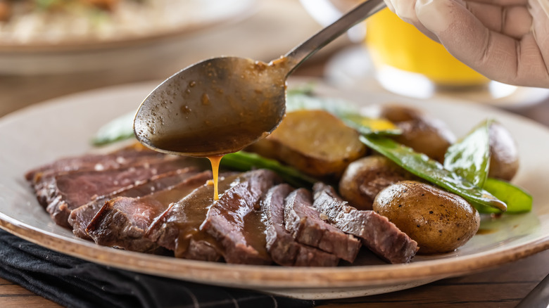 Chef spooning pan sauce over sliced steak