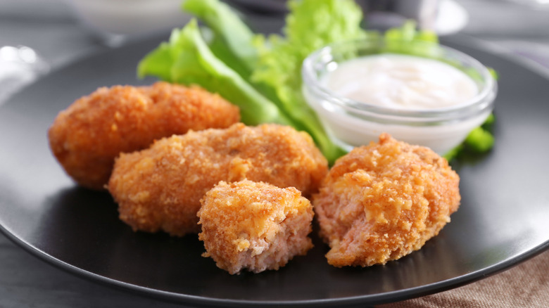 fried salmon croquettes on a black plate with a lettuce leaf and ramekin of white sauce