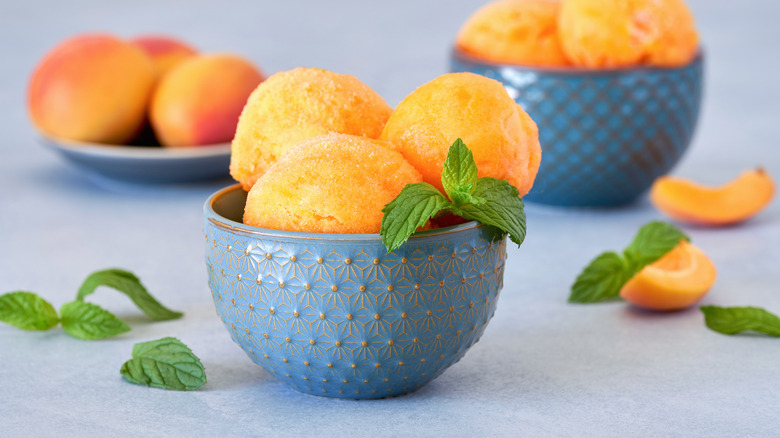 scoops of peach sorbet in blue bowls with mint leaf garnish