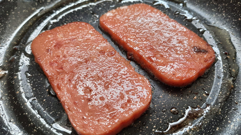 two pieces of Spam frying in a skillet