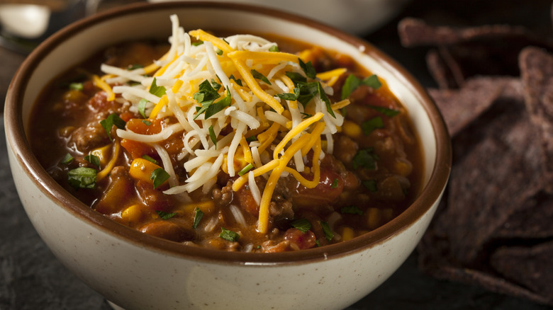 A small bowl of chili with shredded cheese on top of it.