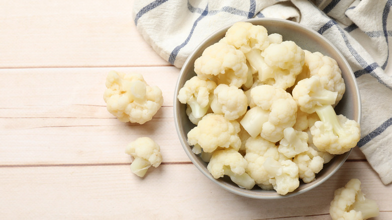 A bowl of cauliflower florets on a white wooden background