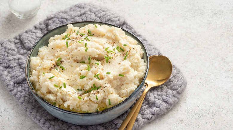 A bowl of mashed cauliflower with chives next to golden spoons