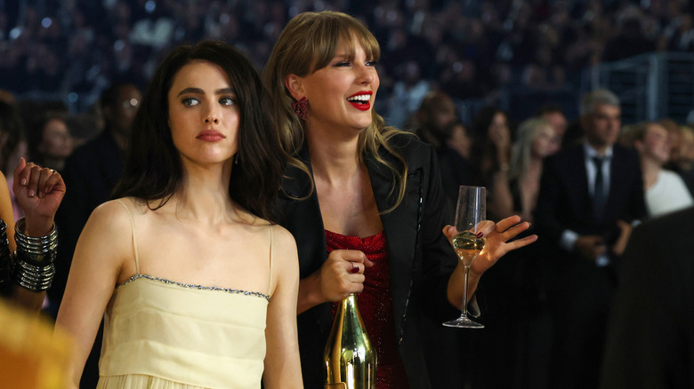 Taylor Swift holding a champagne glass and bottle next to Margaret Qualley at the Grammy's