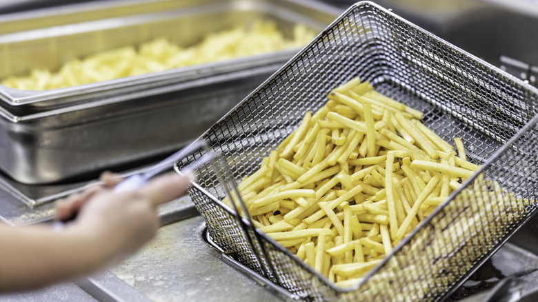 a cook lifting a french fry basket out of the oil