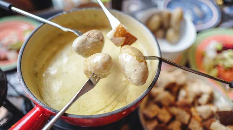 Four forks of potatoes and bread dipping into cheese fondue pot