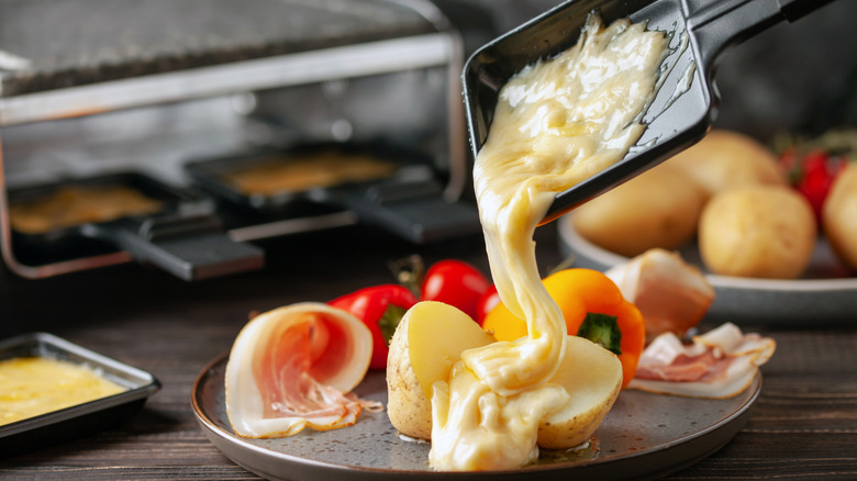 Melted cheese pouring onto plate of potatoes, prosciutto and veggies