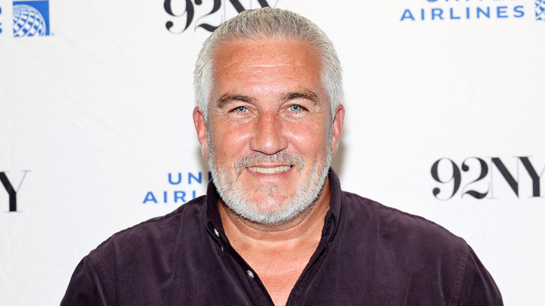 Paul Hollywood smiles in a maroon button down shirt