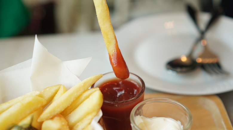 A person dipping a french fry in ketchup.