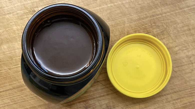 Open jar of Marmite spread with lid on a wooden board