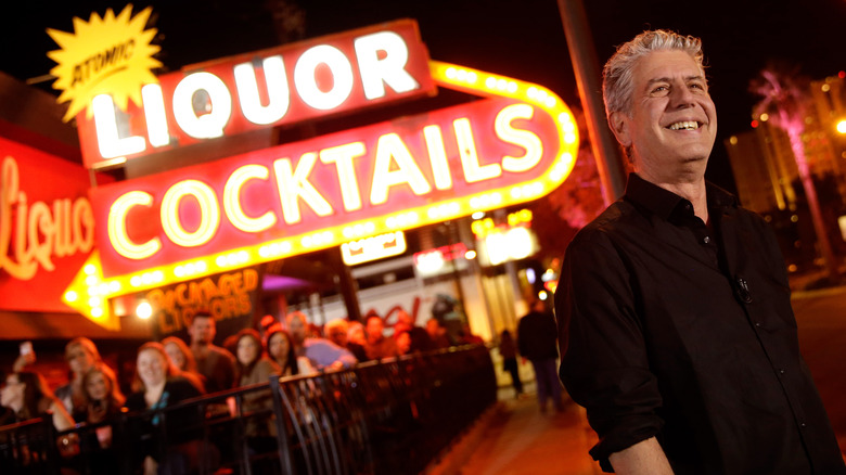 Anthony Bourdain next to giant neon sign at Atomic Liquor