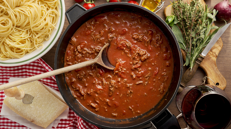 spaghetti sauce in black pot next to white bowl of cooked spaghetti