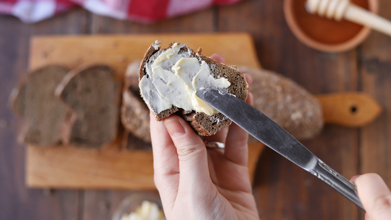 closeup of hand spreading butter on rustic piece of toast