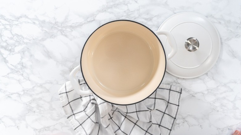 overhead view of white dutch oven pot with lid off near plaid kitchen towel