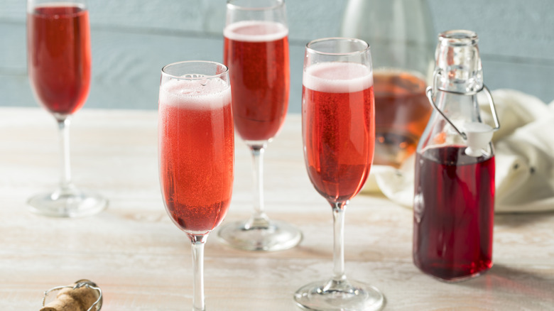 Four red cocktails in champagne glasses beside bottle of red syrup