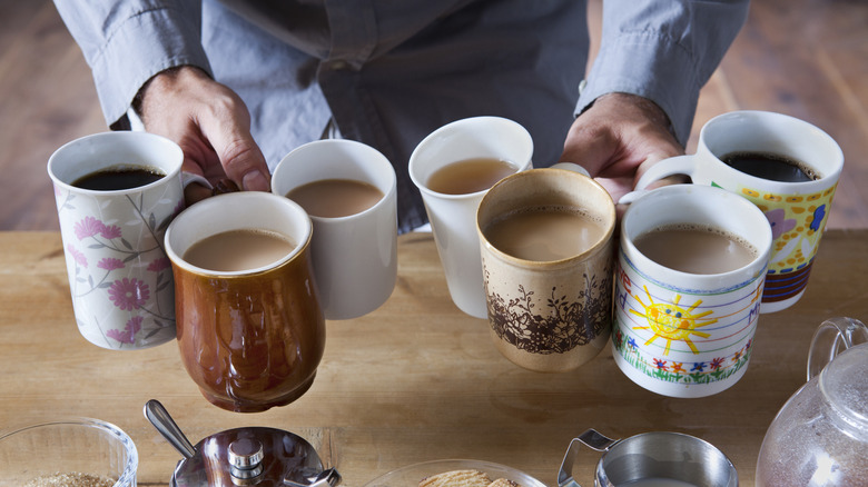 A person carrying multiple mugs of tea and coffee